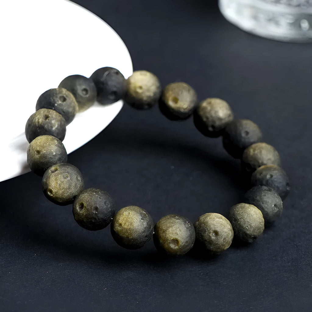 Close-up of an obsidian crater ball bead bracelet in a gold meteorite finish, showing its textured spherical beads.