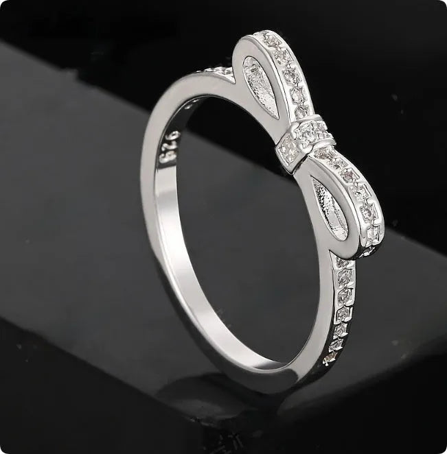 Silver coloured bow-shaped ring with sparkling rhinestone crystals on a model's hand.