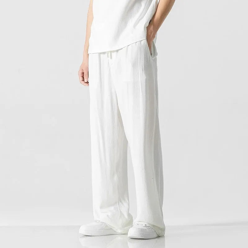 Man wearing beige straight-leg cropped bamboo fibre trousers with a drawstring waist on a summer day.