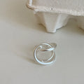 Geometric open ring with a 3D interlaced design in matte gold or silver metal.
