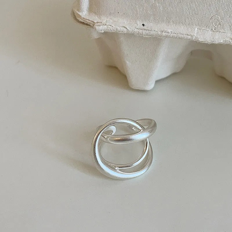 Geometric open ring with a 3D interlaced design in matte gold or silver metal.