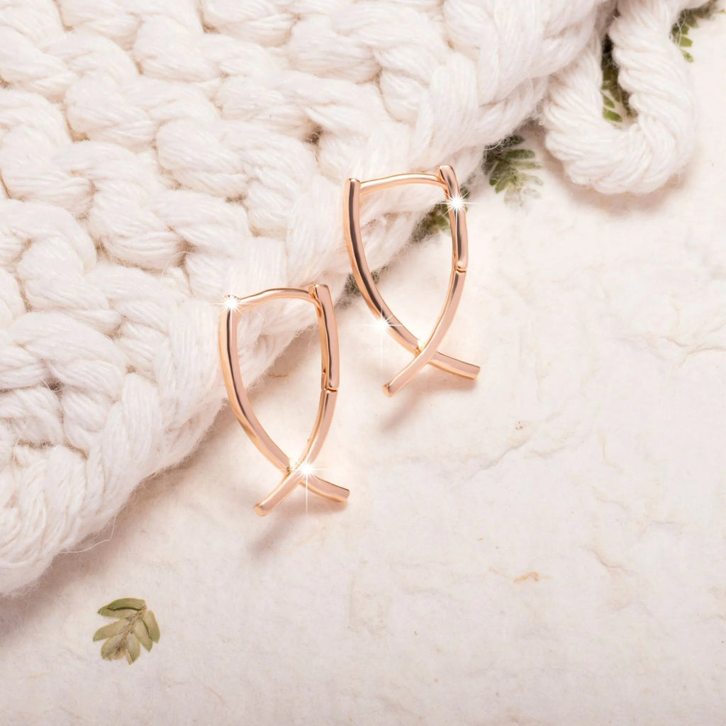 Close-up of a pair of rose gold cross drop earrings on a white background, showing post fittings.