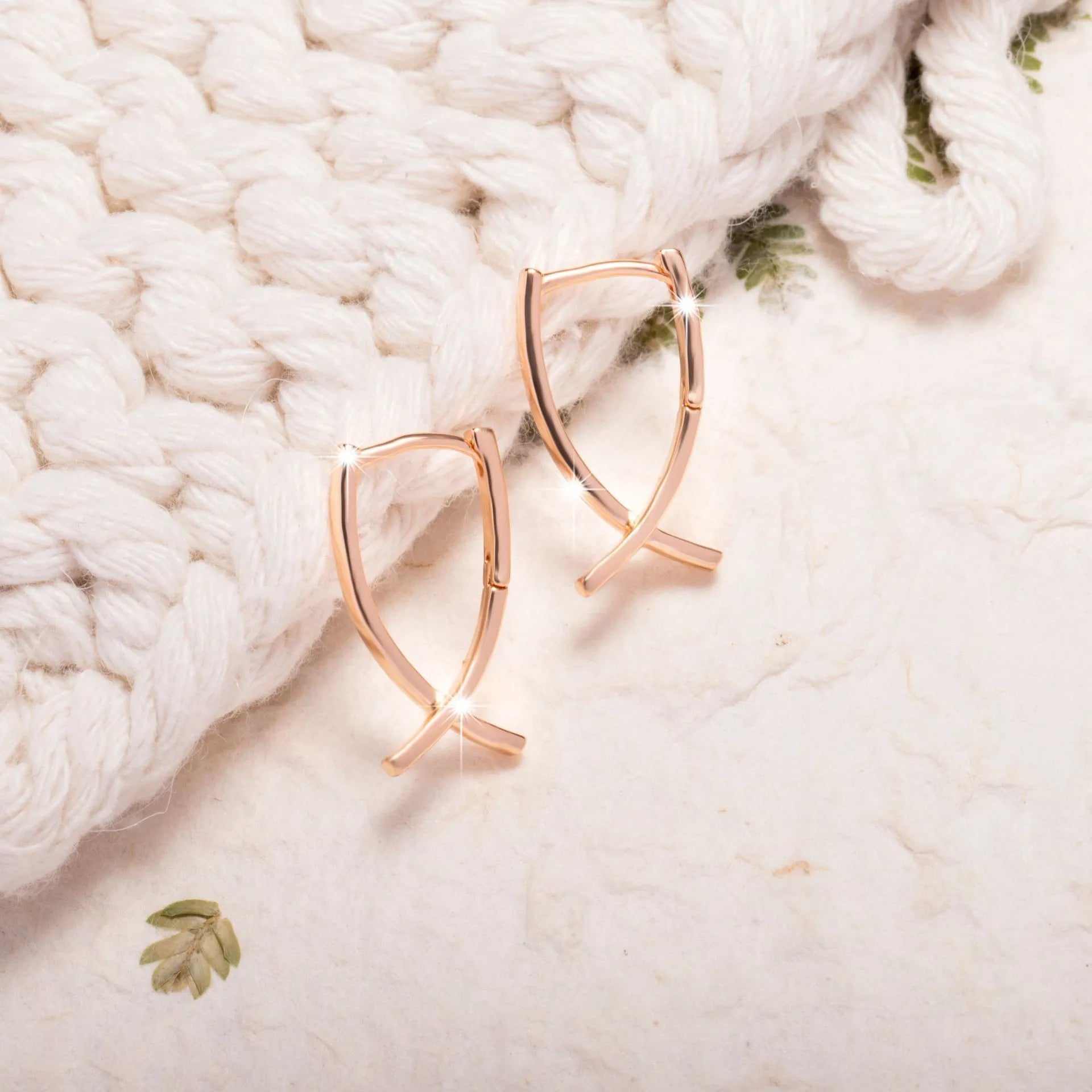 Close-up of a pair of rose gold cross drop earrings on a white background, showing post fittings.