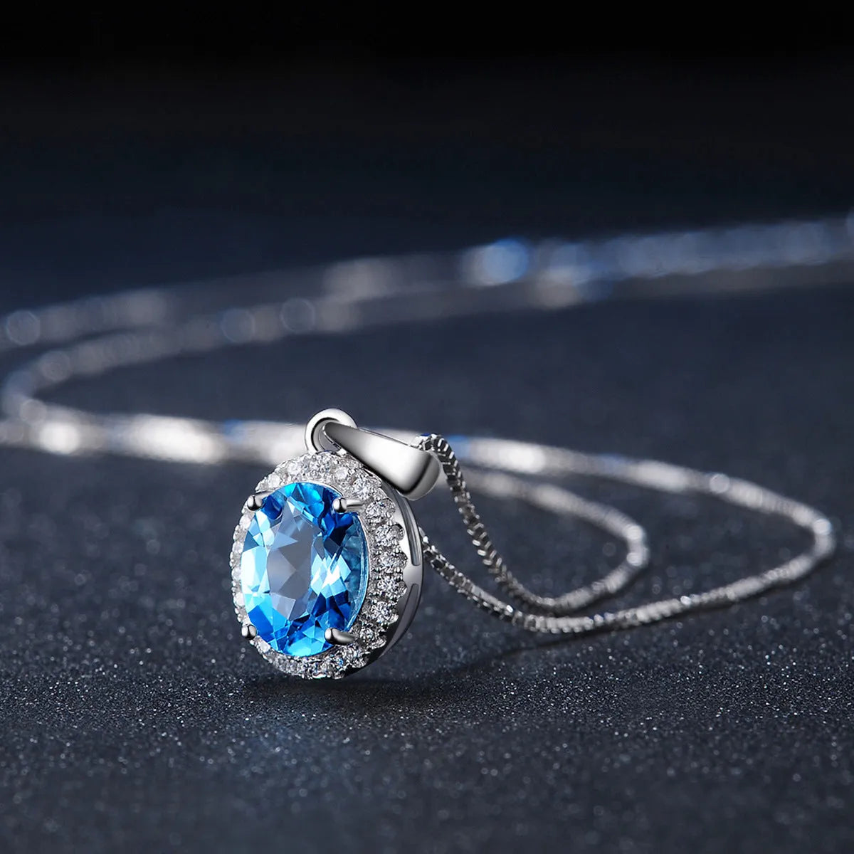 Four-piece sterling silver jewellery set with blue topaz gems: earrings, ring, pendant, and necklace on a geometry pattern.