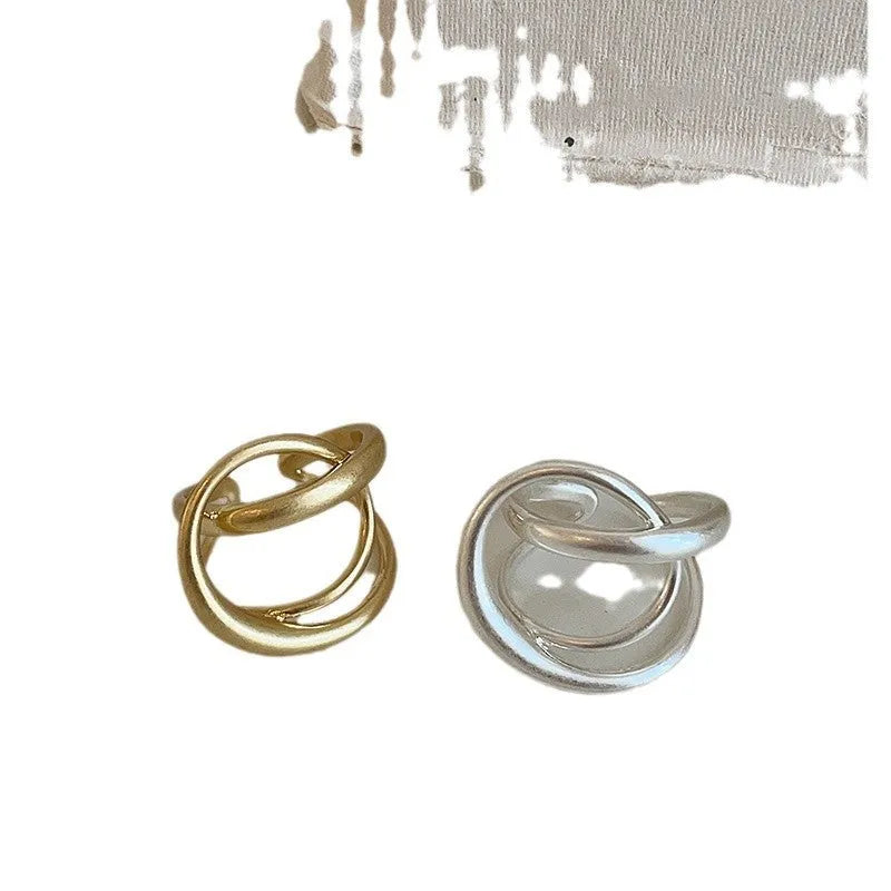 Geometric open ring with a 3D interlaced design in matte gold or silver metal.