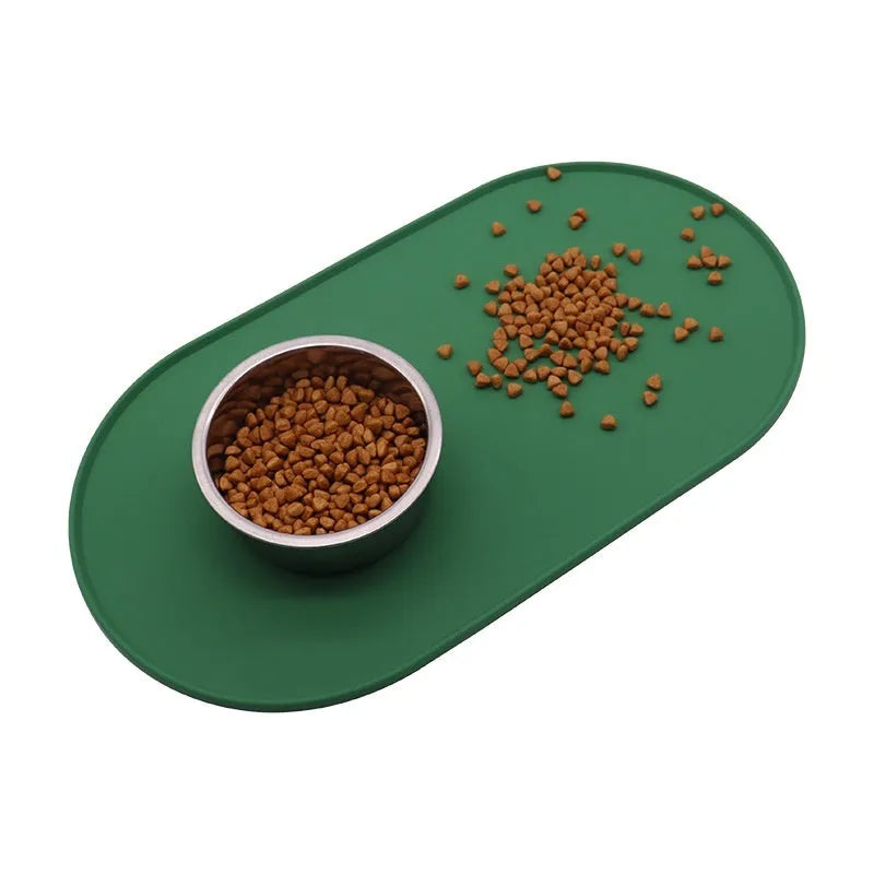 Green silicone cat feeding mat with raised edge holding a food bowl and water bowl on a kitchen floor.
