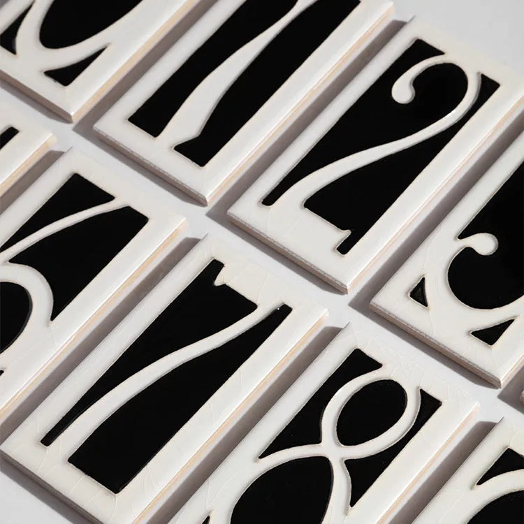 Handmade retro-style ceramic doorplate with fired enamel number, shown against a door.