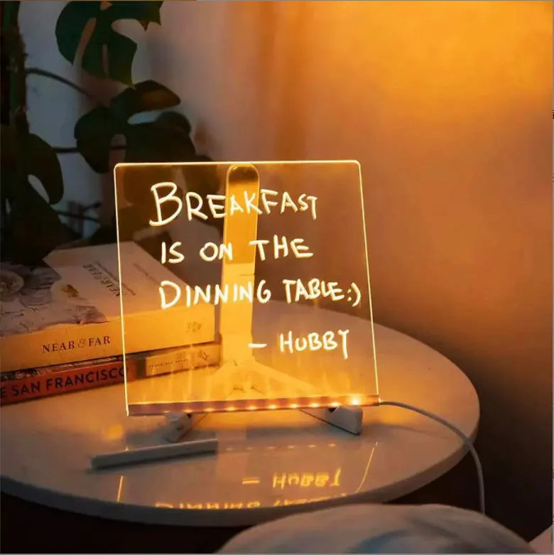 Acrylic DIY LED message board on a bracket, glowing softly with handwritten notes, alongside white and colourful pens.