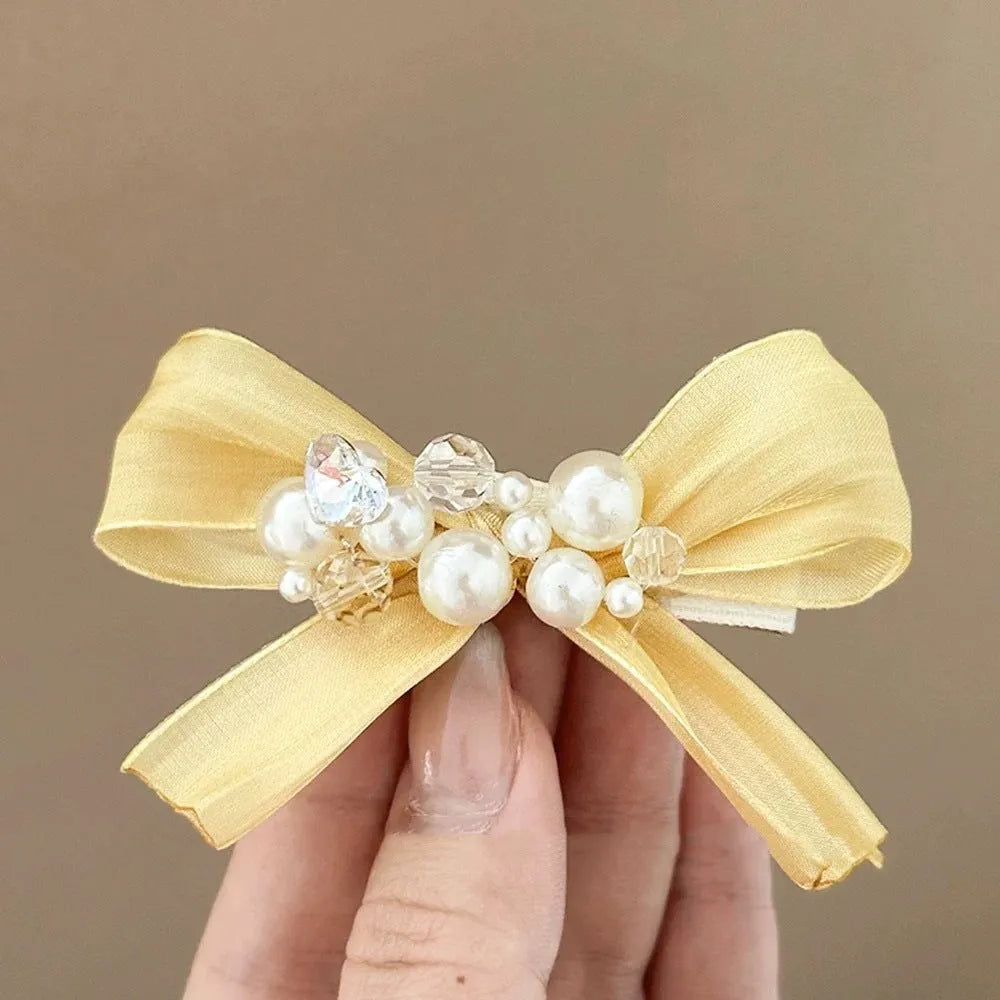 Yellow bow hair barrette with rhinestone and pearl accents on duckbill metal clip