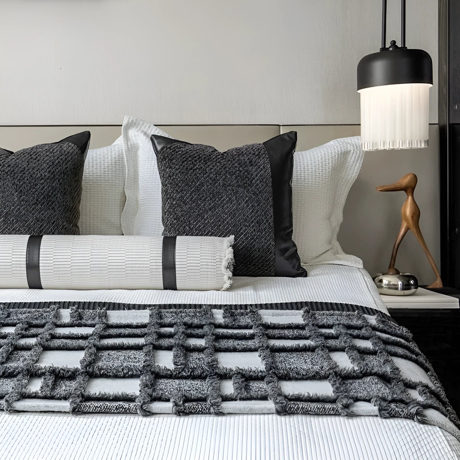 Grey and white plaid bed runner blanket with matching pillowcase and brown leather round pillow on a bed.
