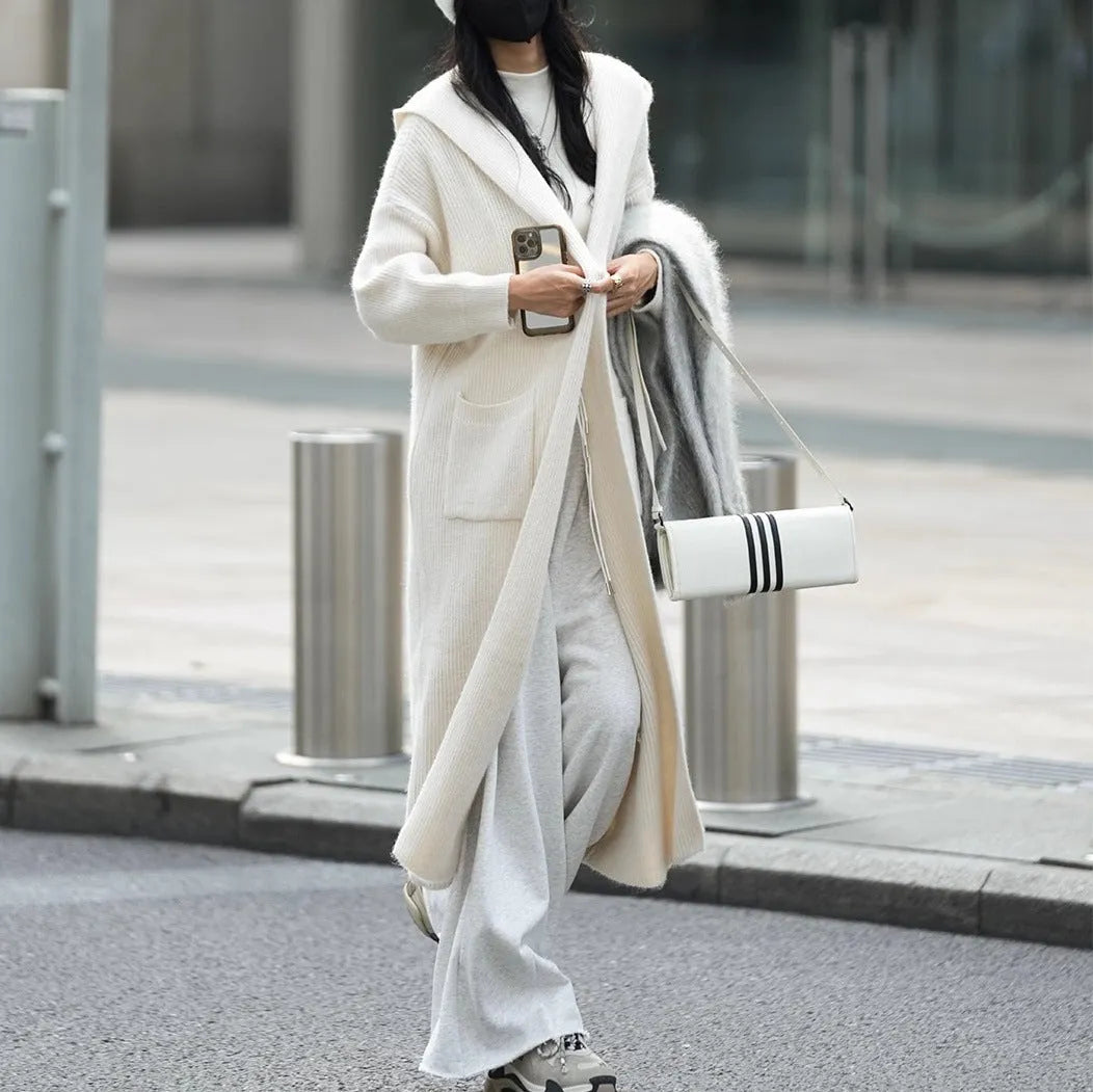 Long grey knitted women's cardigan with hood and trench coat design, shown open as a front-fastening garment.