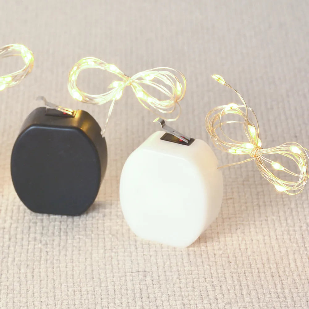 Copper wire LED button light string shaped into a spiral, powered by a small white battery box.