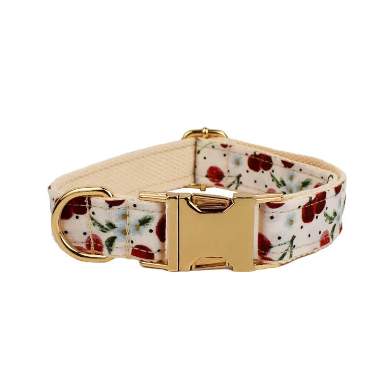 Red cherry print pet collar, lead, and harness set with light gold buckles and matching waste bag dispenser