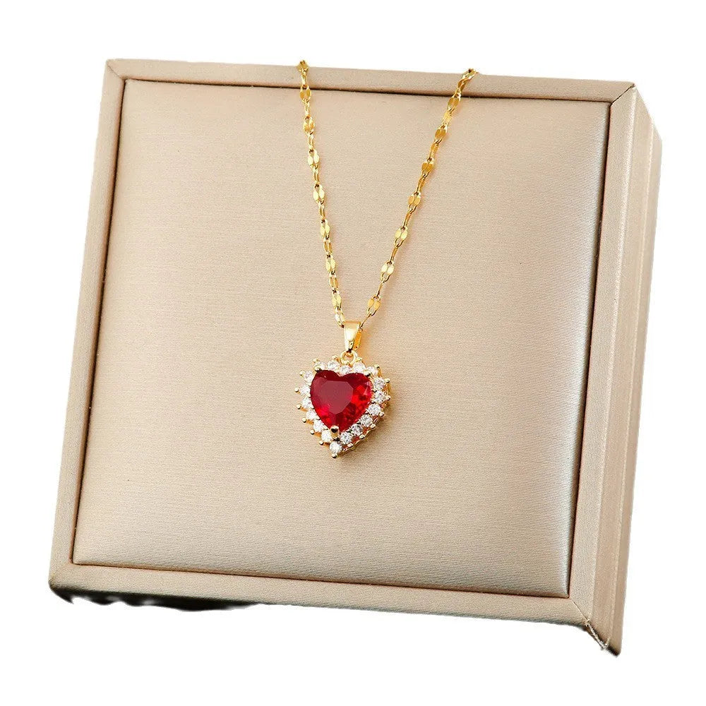Gold red titanium steel necklace with heart and flower pendant, matching stud earrings, and ring on a grey background.