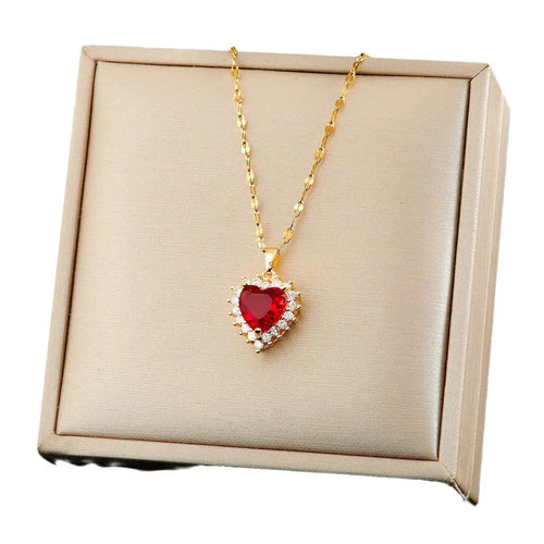 Gold red titanium steel necklace with heart and flower pendant, matching stud earrings, and ring on a grey background.