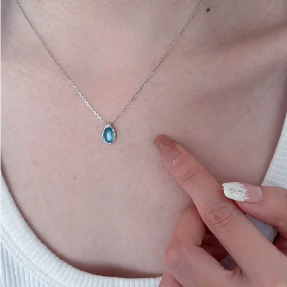 Close-up of a navy blue and platinum coloured water drop pendant necklace with an adjustable cross chain on a person's collarbone.