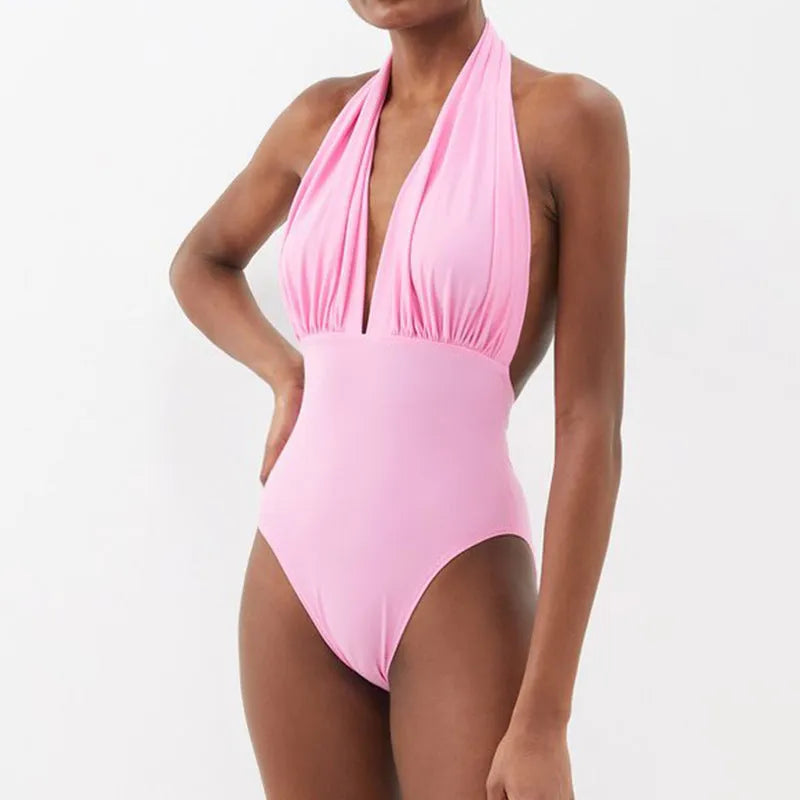 Solid colour women's one-piece swimsuit with deep V halter neck and backless design, shown with matching skirt.
