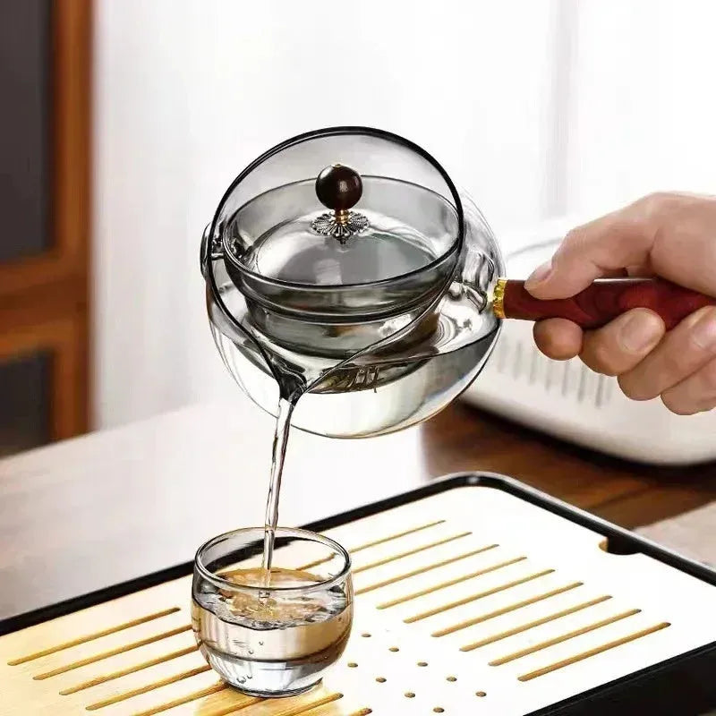 Grey and transparent rotary glass teapot with wooden handle and infuser on a kitchen counter