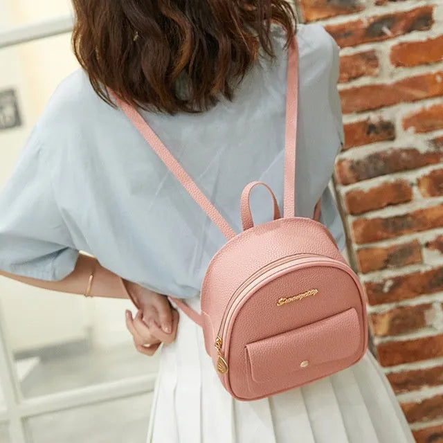 Small black PU women's backpack worn on shoulder, showing zip closure and compact size.