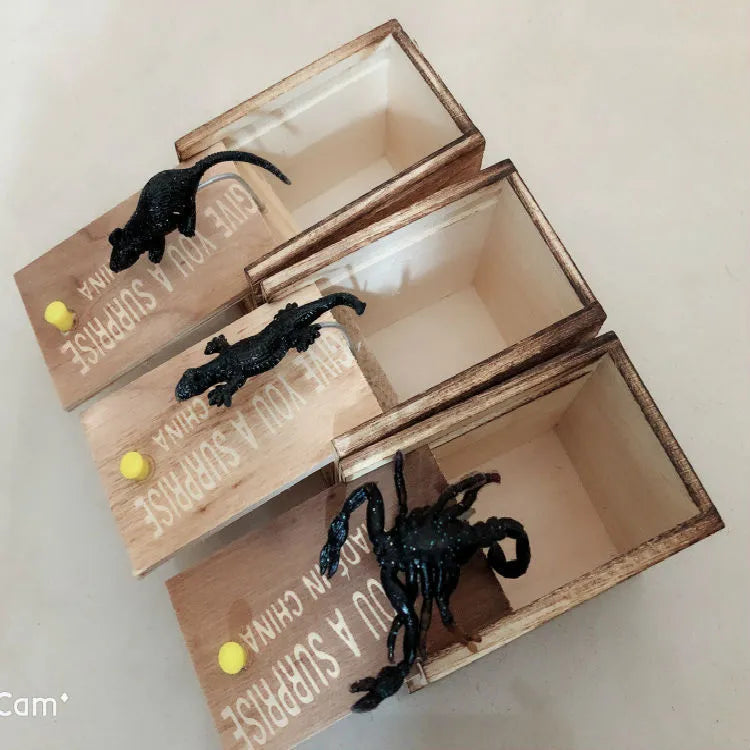 Wooden prank scare box closed, with a lifelike jumping spider toy next to it.