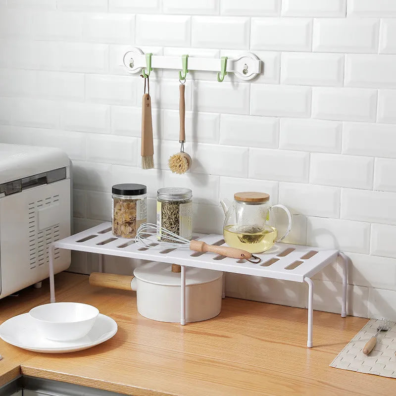 White telescopic plastic storage rack extended to full height with kitchen utensils organised on shelf