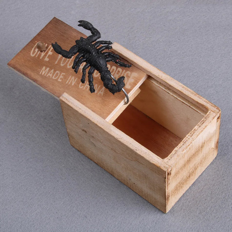 Wooden prank scare box closed, with a lifelike jumping spider toy next to it.