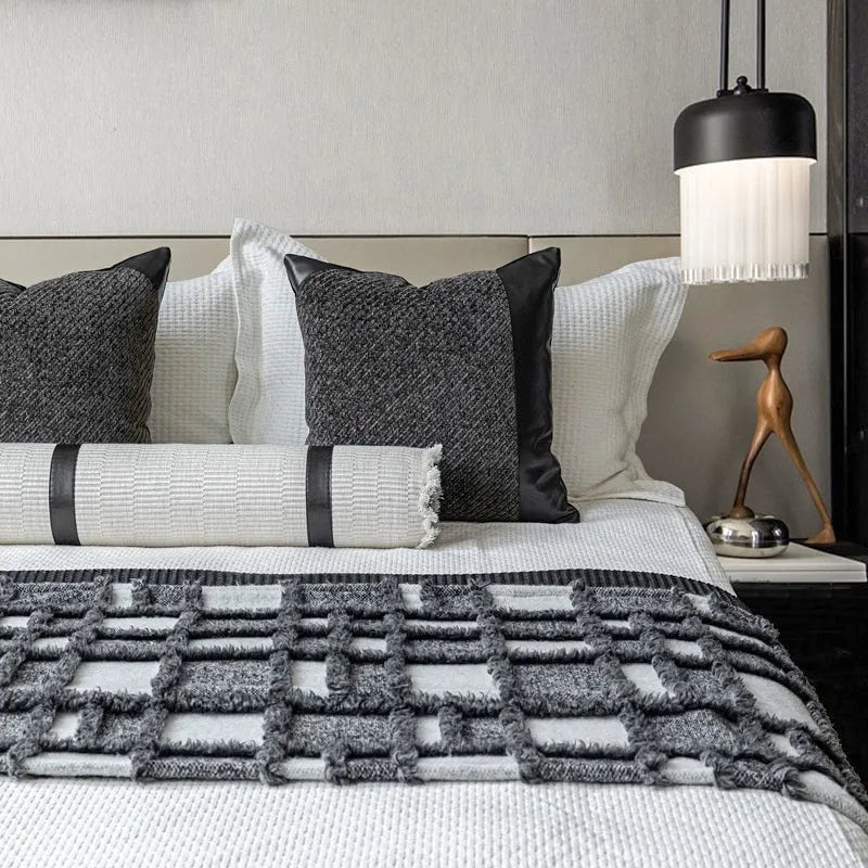 Grey and white plaid bed runner blanket with matching pillowcase and brown leather round pillow on a bed.