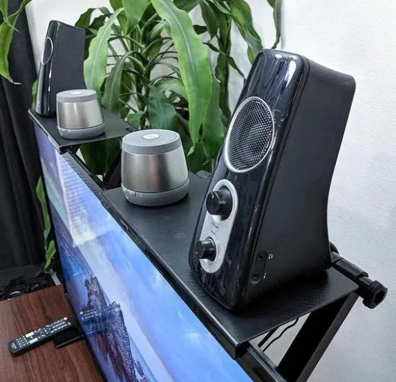 Black adjustable screen top shelf on a desktop monitor holding a streaming device and remote