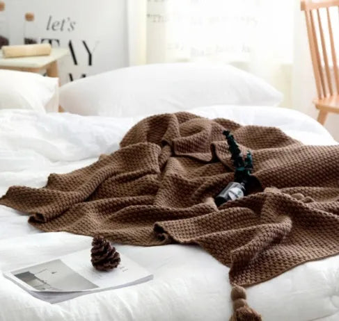 Nordic-style knit blanket with fringe trim in a neutral colour on a sofa