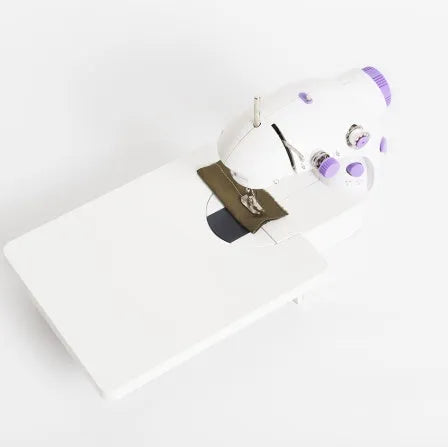 Small white plastic electric sewing machine with thread cutter and light on a table