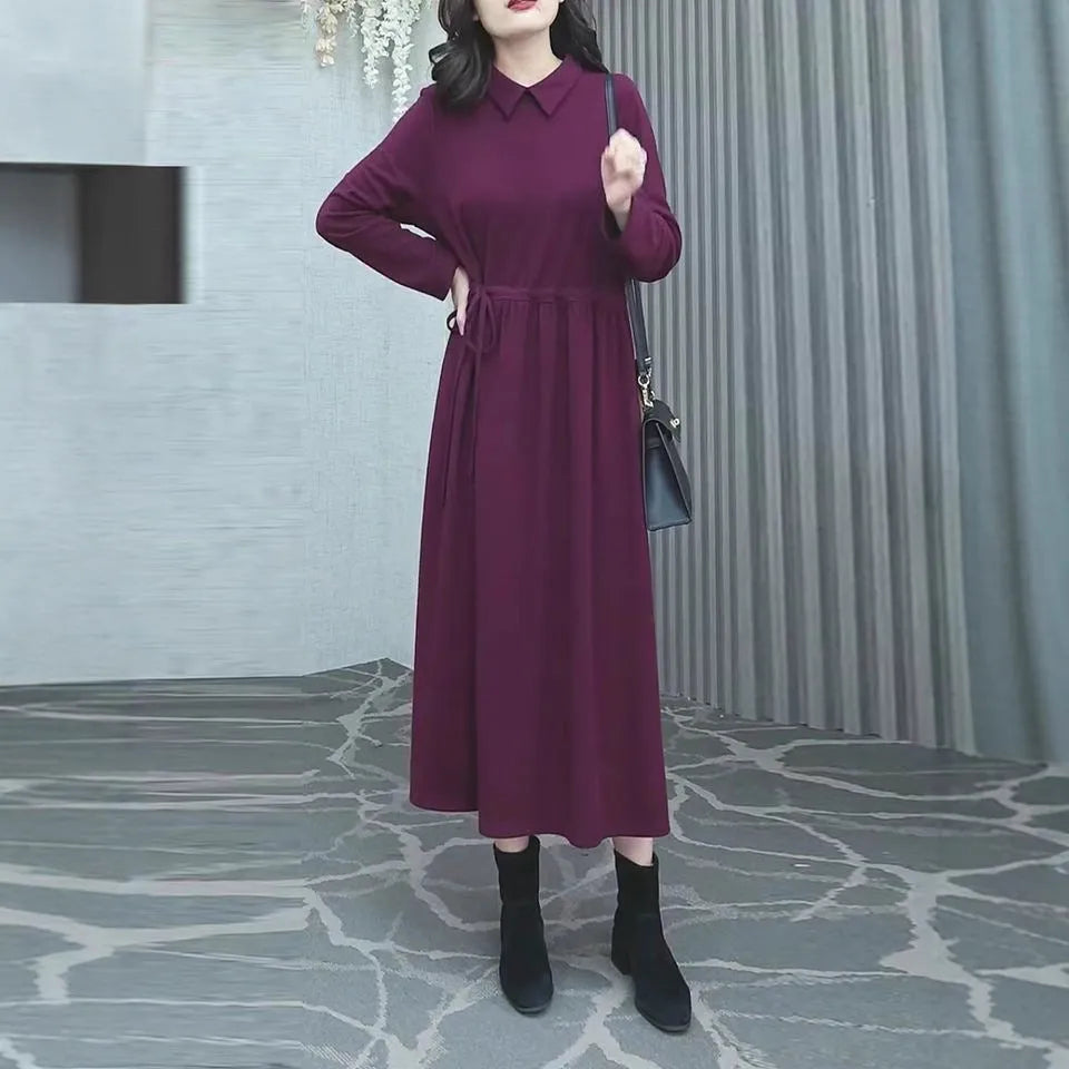 A woman wearing a solid purplish-red long-sleeve maxi dress, showcasing its extra-long sleeves and full-length skirt.