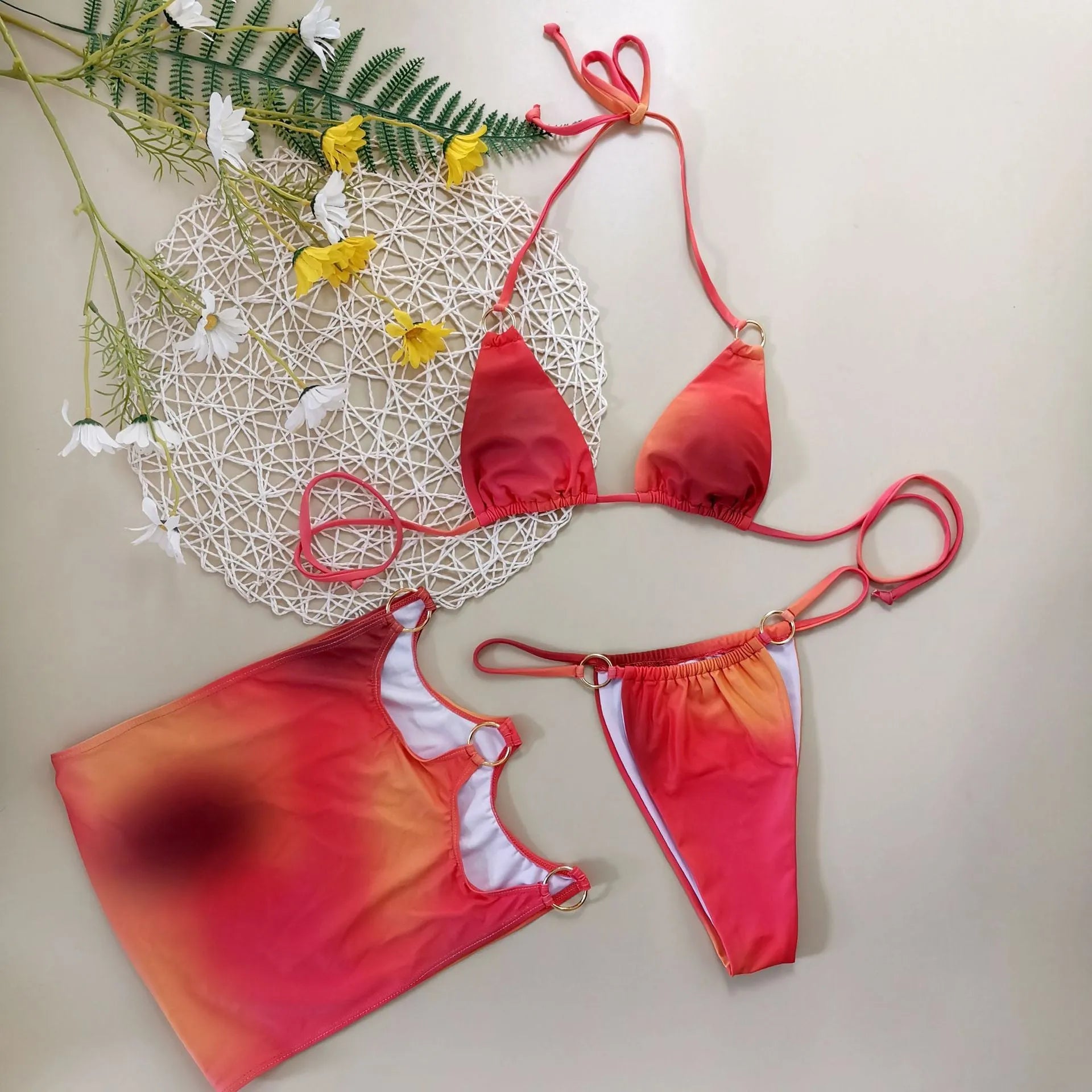 Tie-dye gradient three-piece women's bikini set with halter neck top, briefs, and matching skirt on a neutral background.