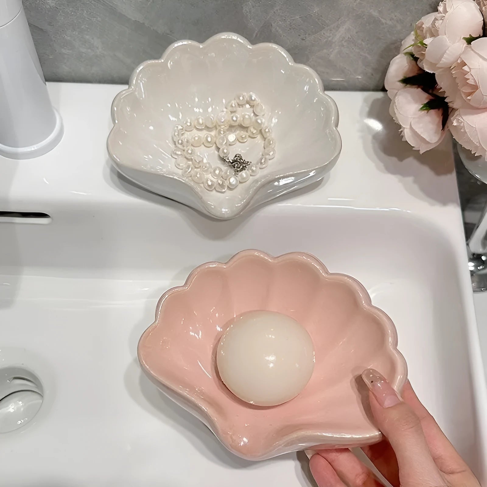 White or pink plastic shell-shaped soap dish for bathroom use on a counter.