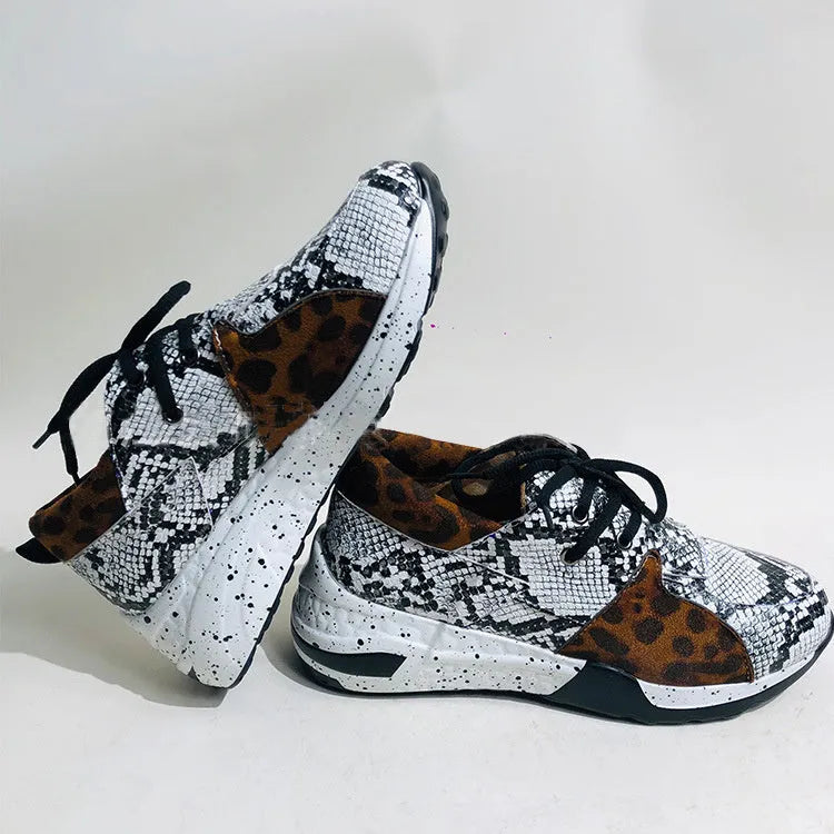 Women's black suede wedge sneakers with a round toe and low-cut design on a wooden floor.