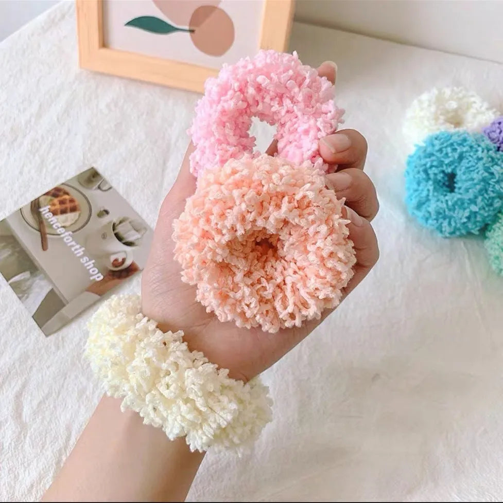 Seven luminous cloth hair ties in blue, pink, green, yellow, orange, purple, and white on a surface