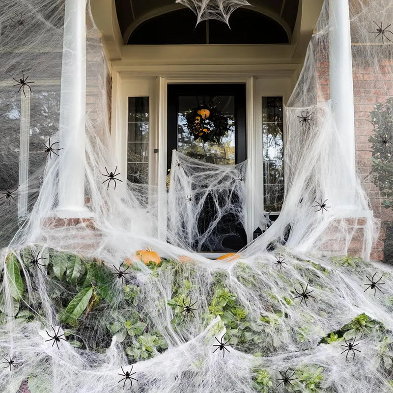 White cotton spider web Halloween decoration with plastic spiders draped over a fence.