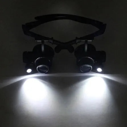 Black double eye magnifier glasses with LED lights and four sets of interchangeable lenses on a headband.