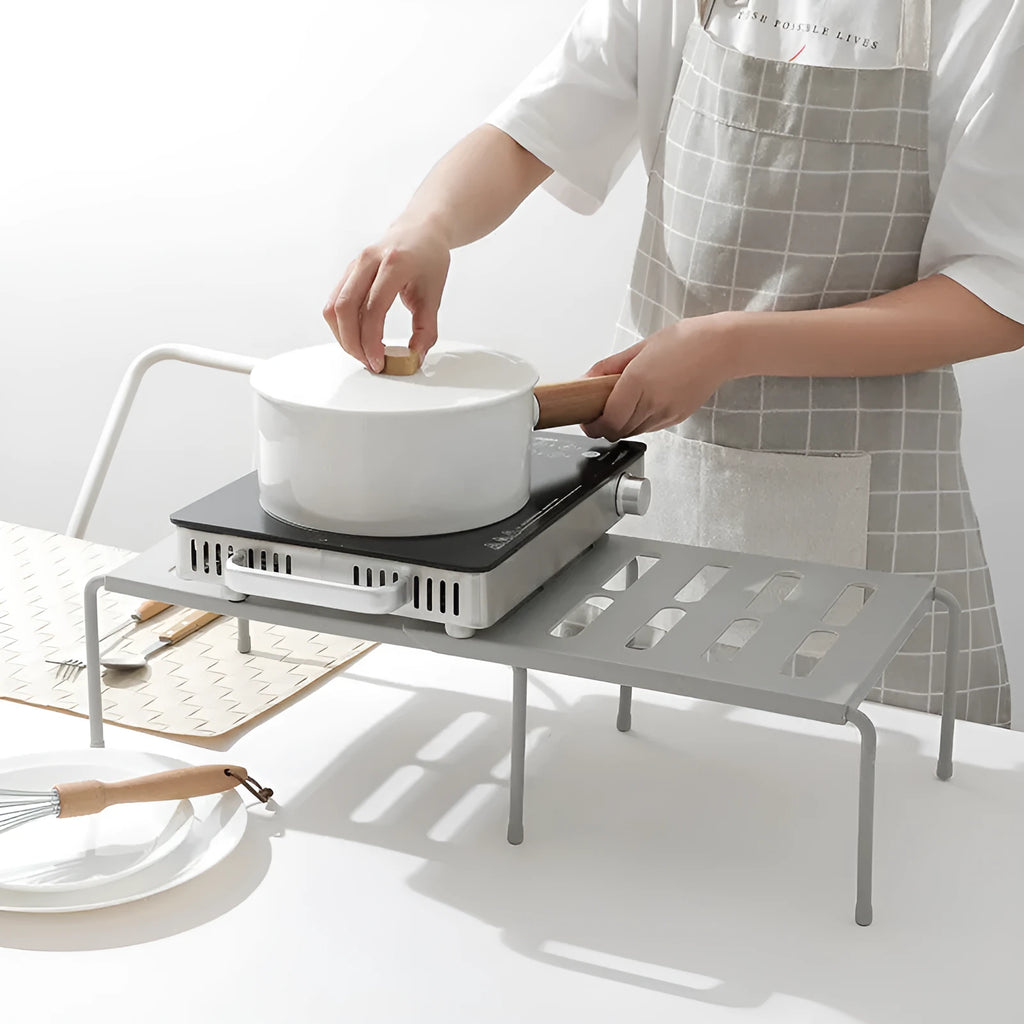 White telescopic plastic storage rack extended to full height with kitchen utensils organised on shelf