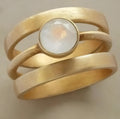 A gold-plated geometric ring with a hollow design and a small white chalcedony stone set into the band.