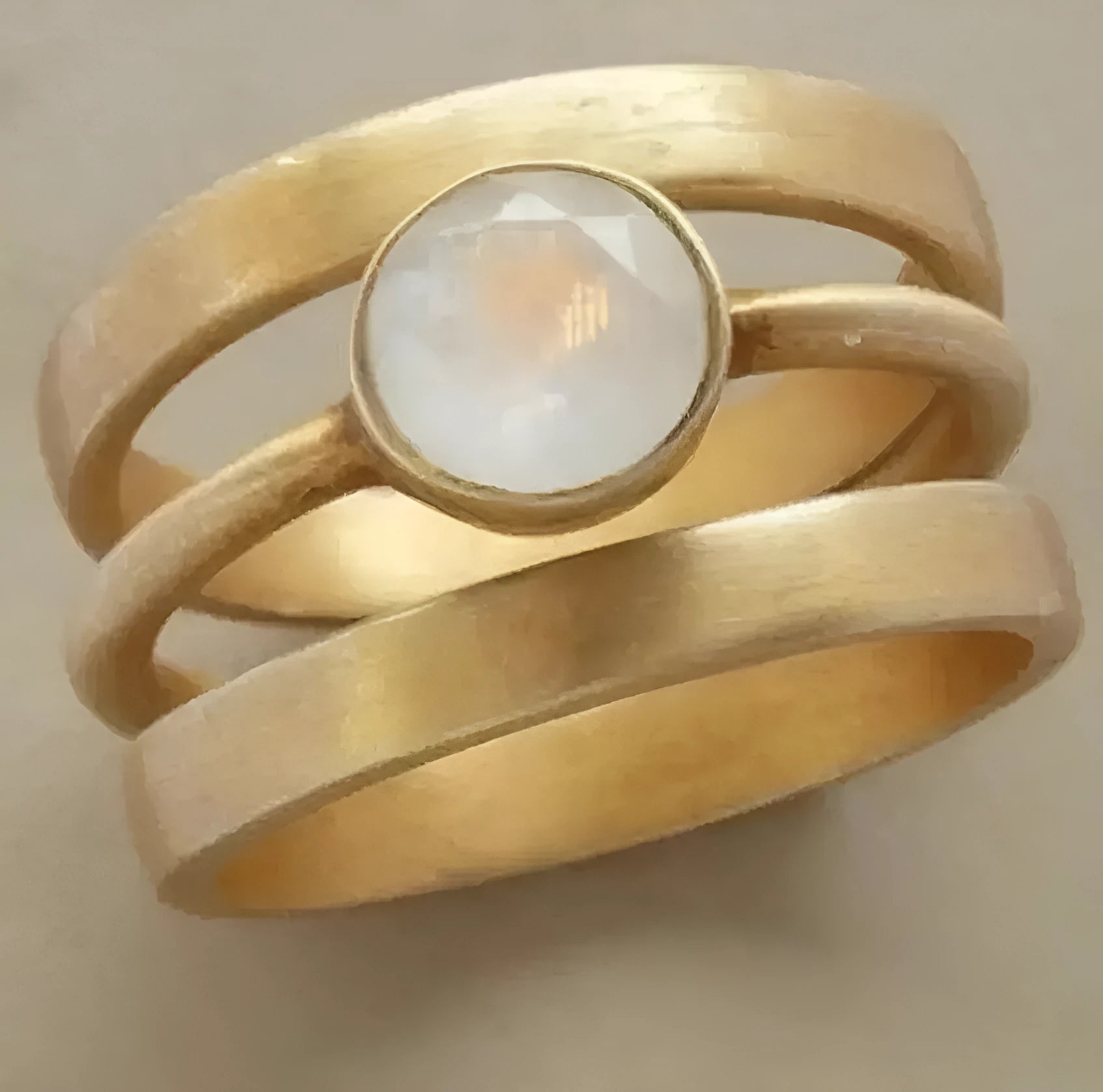 A gold-plated geometric ring with a hollow design and a small white chalcedony stone set into the band.