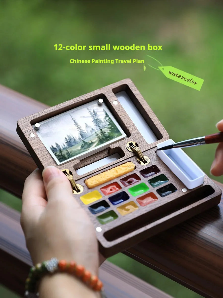 Mini walnut-finished wooden watercolour paint box open to show pigment suit pans inside.