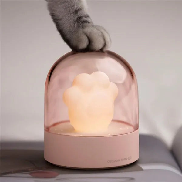 Pink cat paw shaped USB rechargeable night light with soft glow on a desk.