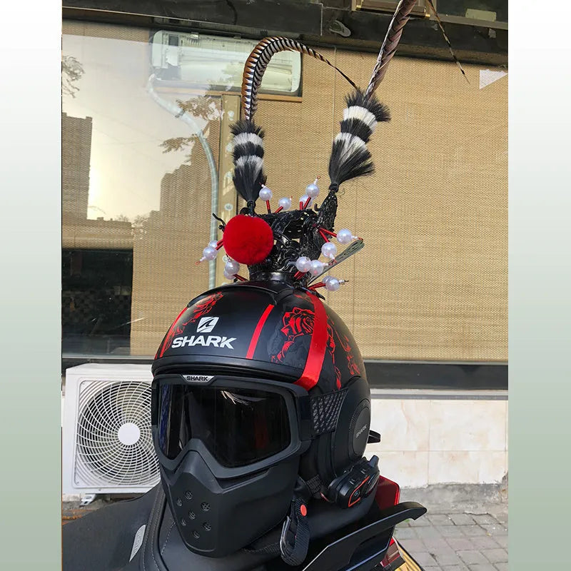 Gold-plated crown ornament with long black feather on motorcycle helmet, showing clip-on leather strap.