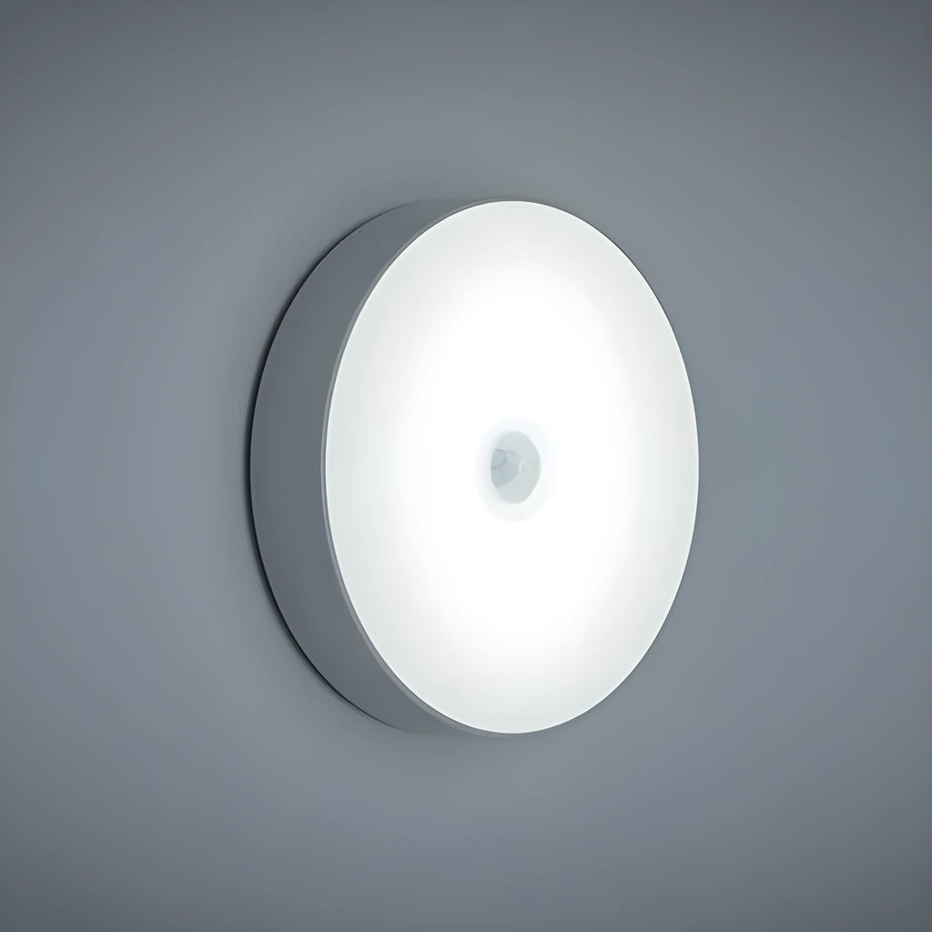 Small white circular LED body sensing night light with USB charging cable and adhesive tape.