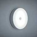 Small white circular LED body sensing night light with USB charging cable and adhesive tape.