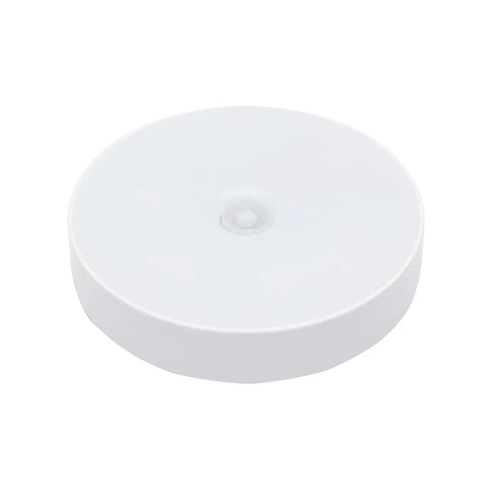 Small white circular LED body sensing night light with USB charging cable and adhesive tape.