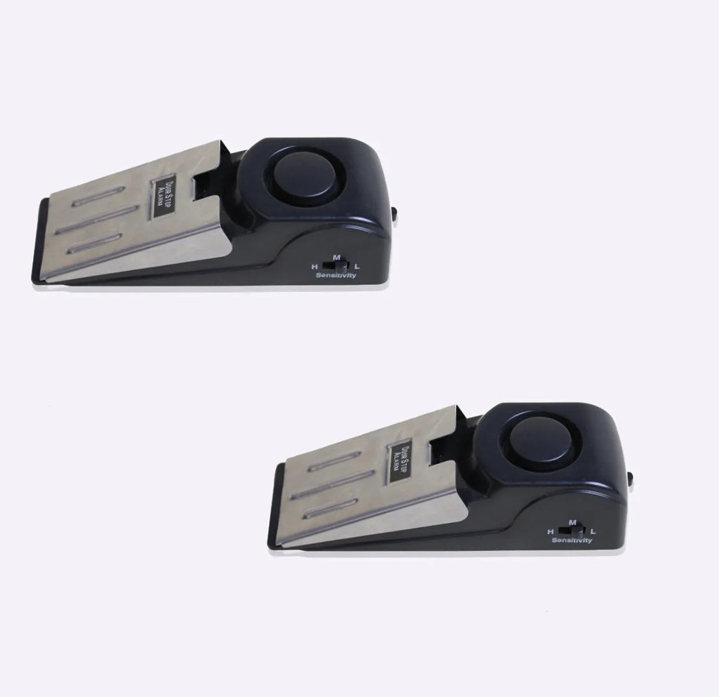 Black portable door stop alarm with wedge shape and stainless steel cover on a wooden floor.