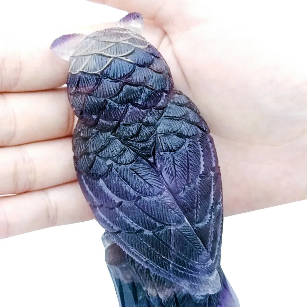 Hand-carved purple fluorite owl ornament on display surface showing natural colour variations