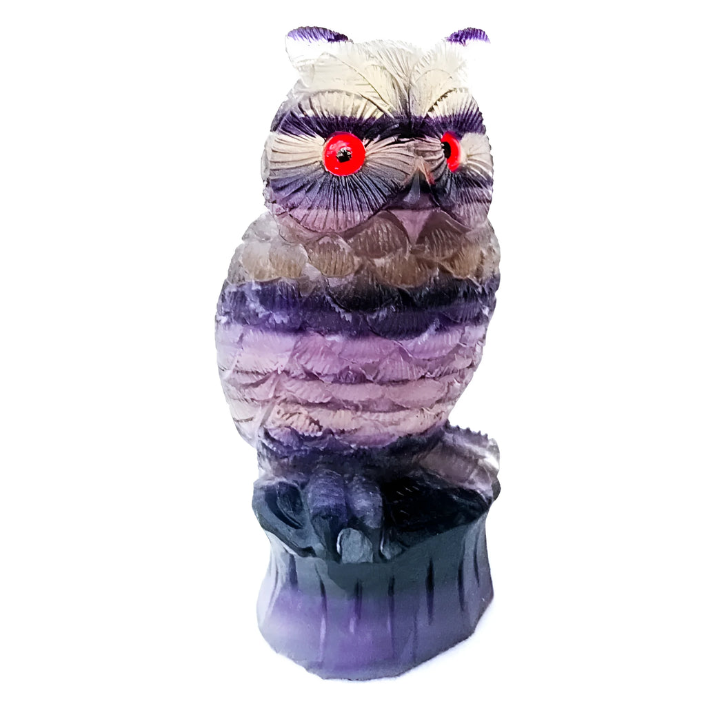 Hand-carved purple fluorite owl ornament on display surface showing natural colour variations