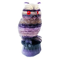 Hand-carved purple fluorite owl ornament on display surface showing natural colour variations
